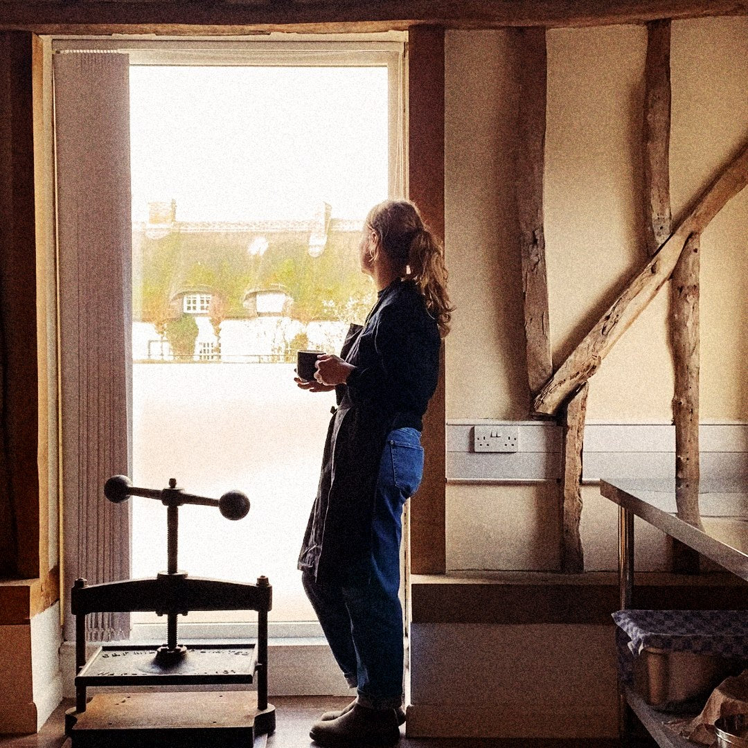 Metta's founder at the workshop window, a mug of tea in hand — a quiet moment after blending.