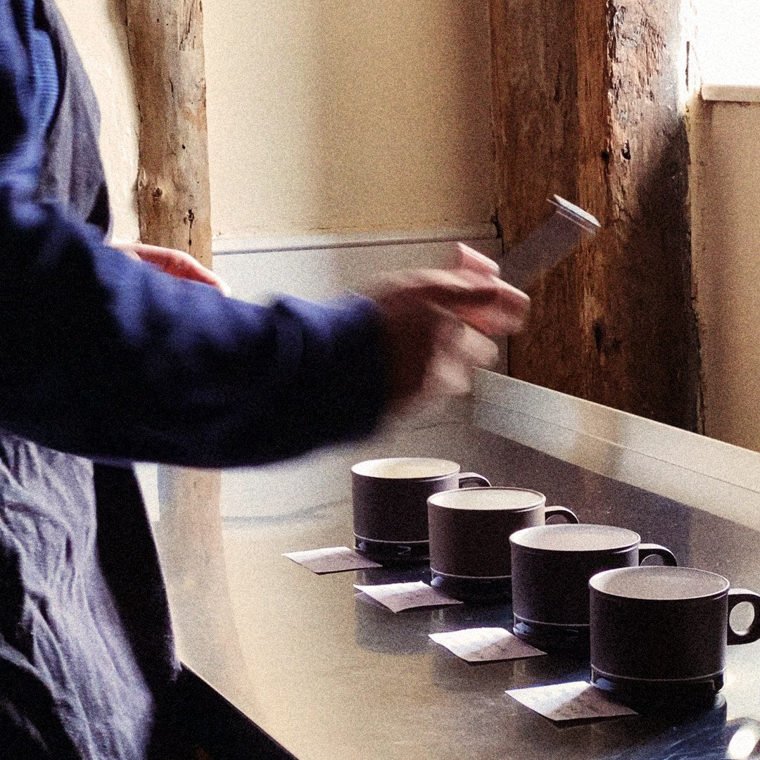 Metta's founder writing up tasting labels on four ceramic mugs lined up on a counter.