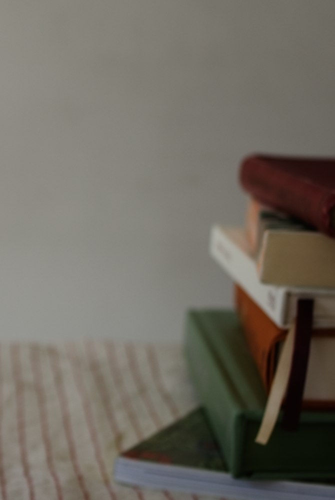 A stack of hardback books on a striped linen runner — spines catching soft window light.