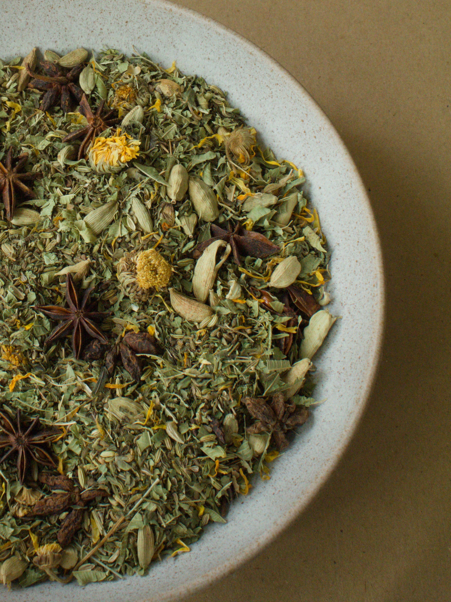 Gut Feeling loose-leaf blend — star anise and cardamom pods among fennel seeds and marigold petals in a stoneware bowl.