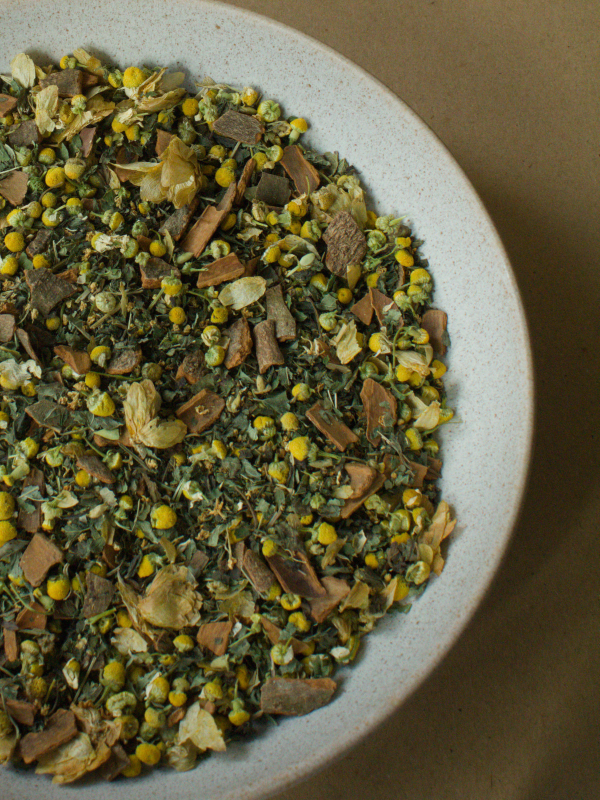Good Night loose-leaf blend — chamomile flowers, hops, cinnamon bark and elderflower in a stoneware bowl, in close-up.