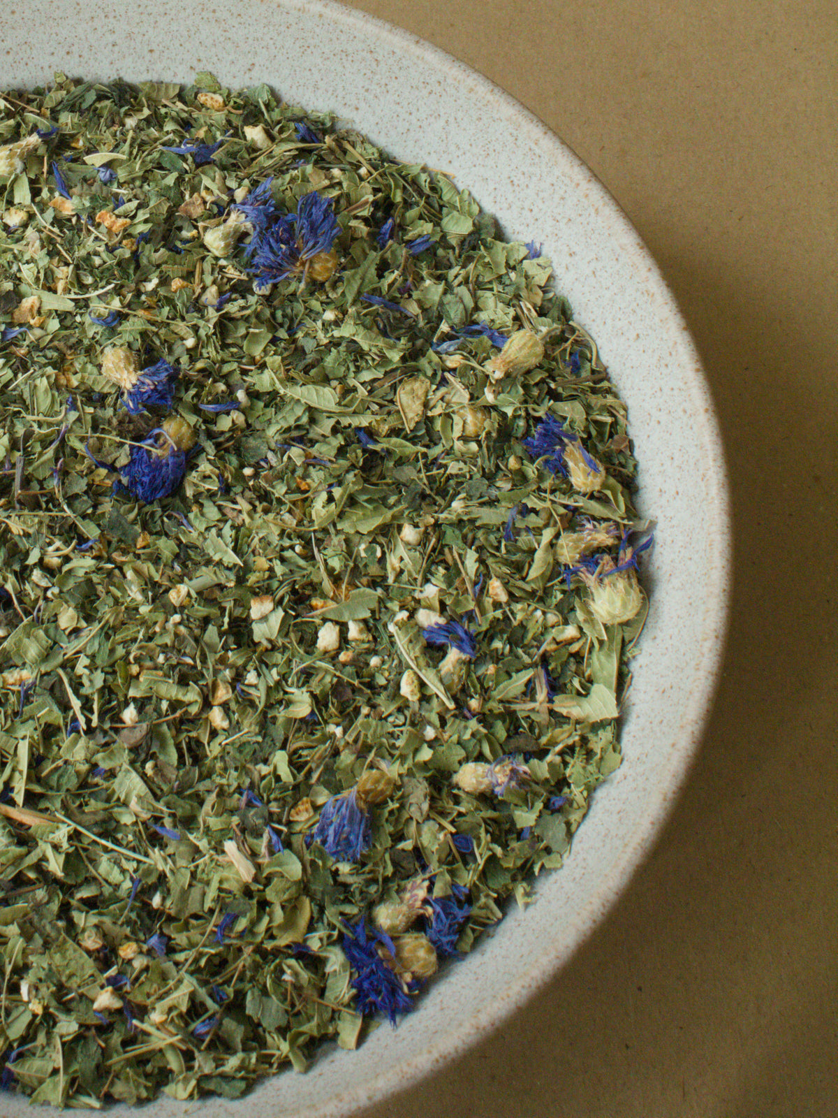 A Sense of Ease loose-leaf blend — blue cornflower petals and orange peel scattered through the herbs in a stoneware bowl.