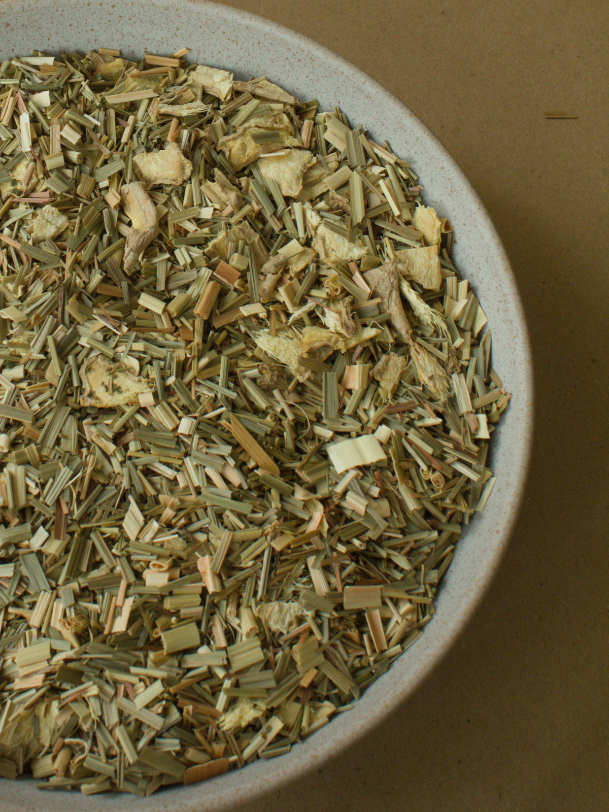 Good Morning loose-leaf blend — pale lemongrass strands and dried ginger in a stoneware bowl, closely observed.