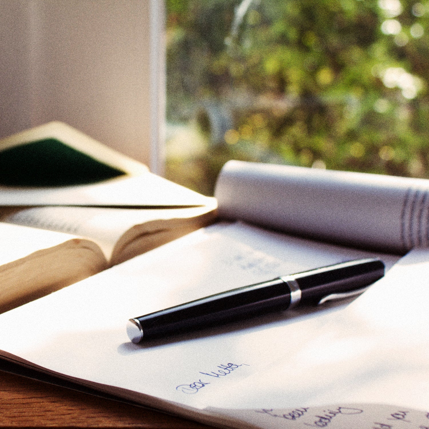 A fountain pen on an open notebook — mid-letter, garden greenery soft and out of focus beyond.