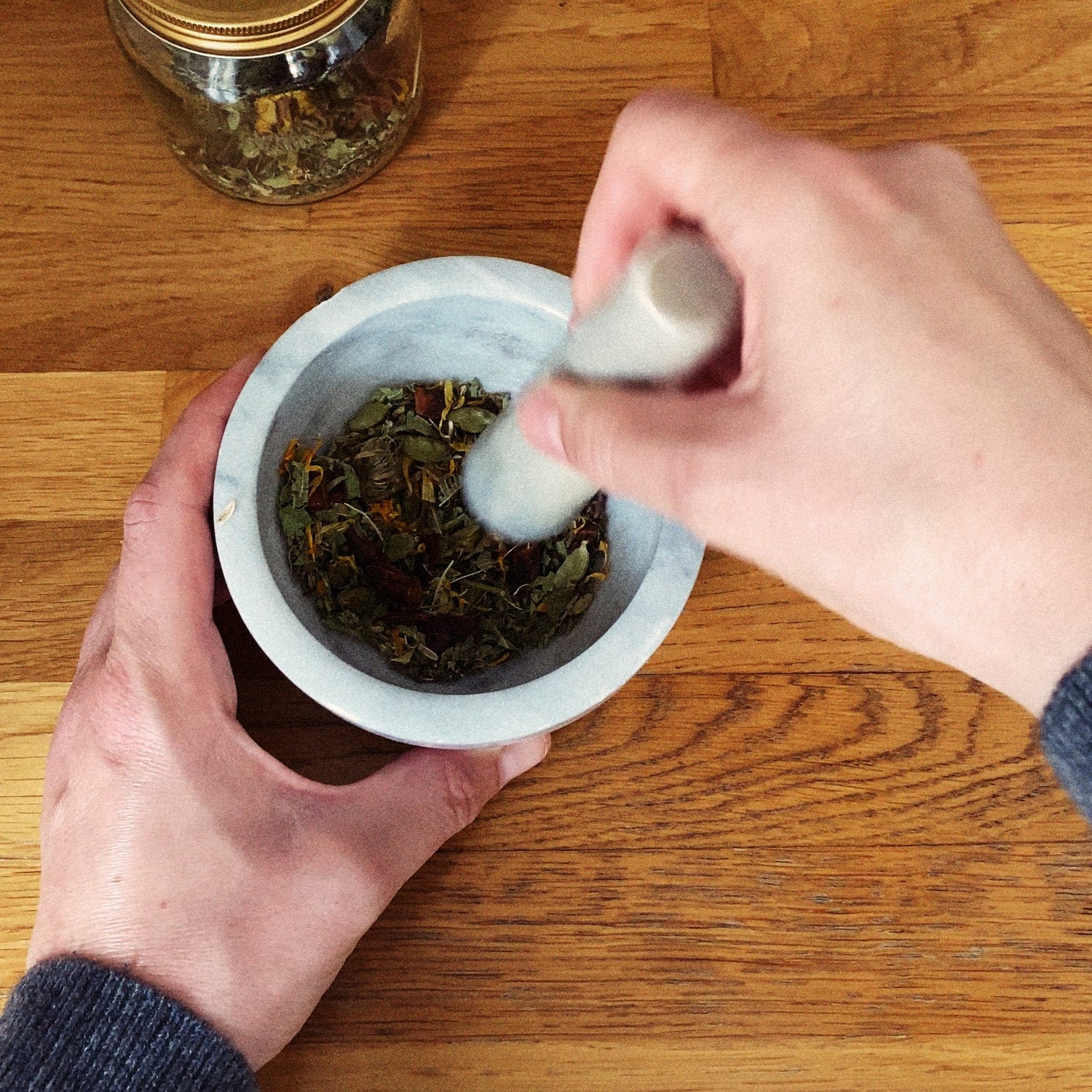 Close-up of hands at work — grinding a small blend of dried herbs in a marble pestle and mortar.